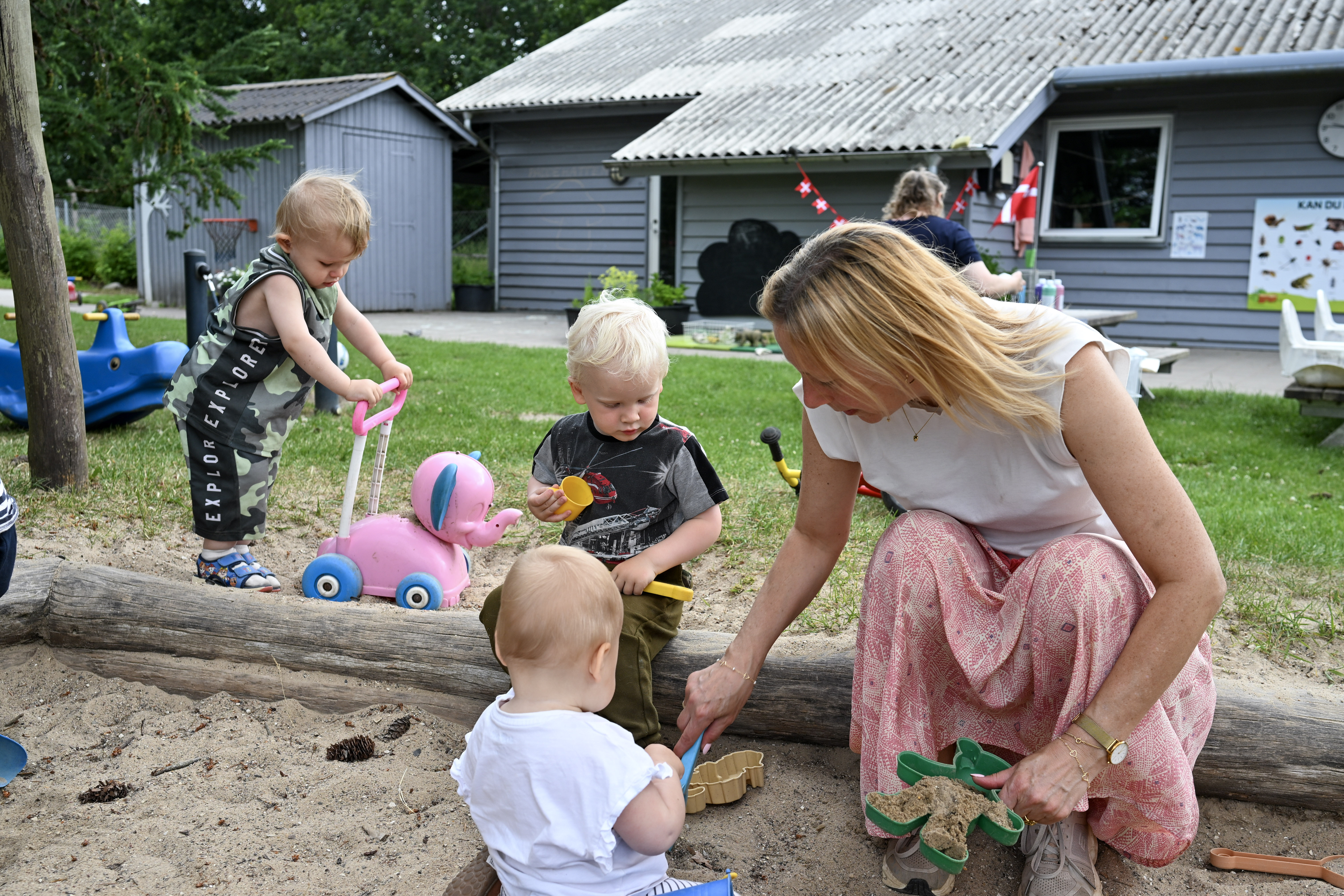 Børn og voksen leger i sandkasse